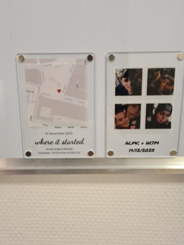 Kunde zeigt zwei personalisierte "Retro Foto's"-Acrylmagnete an einer weißen Tafel, einen mit einer Karte und einen mit vier Fotos.