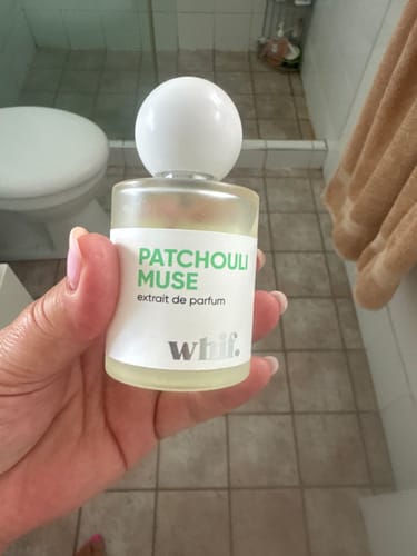Customer holding the clear bottle of Patchouli Muse perfume with its round white cap.