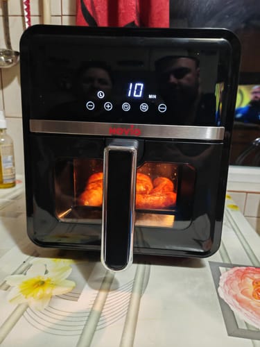 Recenzent folosind friteuza Air Fryer Novio StonePro în bucătărie. Mâncarea se coace în interior, iar ecranul arată 10 minute.