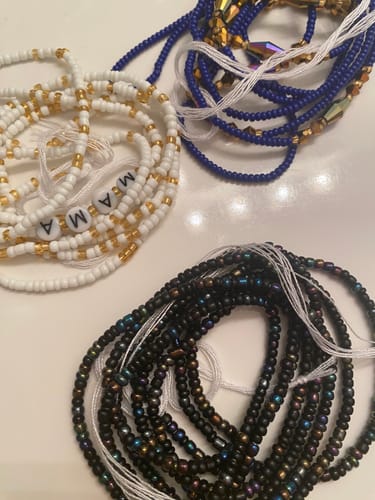 Customer's coiled Black is Beautiful Tie On Waist Beads shown next to white and blue waist beads on a surface.