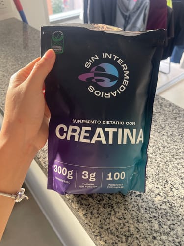 Reseñador sosteniendo en la mano el empaque negro de Creatina Monohidrato sobre una encimera de cocina.