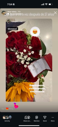 Reviewer's 14K Oval Cut Moissanite Engagement Ring in its open red box, displayed with a beautiful bouquet of roses and a sunflower.