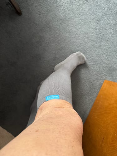 Customer's view of their leg wearing a gray Performance Eucalyptus Compression Sock indoors on a carpeted floor.