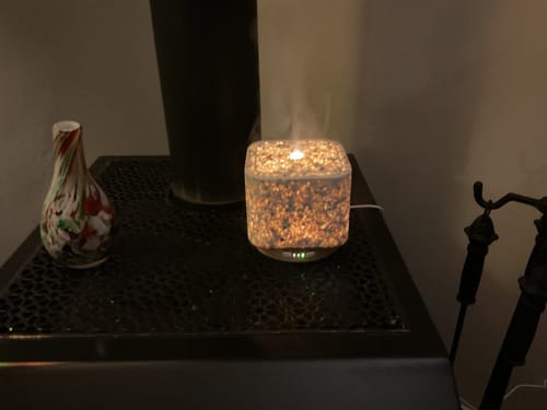 Recensent's Geurwolkje Aroma Diffuser staat aan in een donkere kamer. De verlichte terrazzo kubus verspreidt een zacht wolkje stoom.