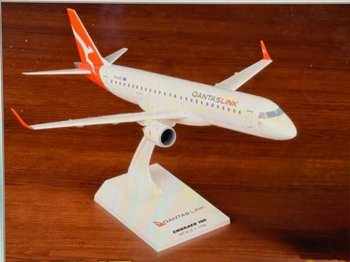 Customer's SKYMARKS QANTAS E190 1/100 model airplane assembled on its display stand, viewed from the side on a wooden surface.