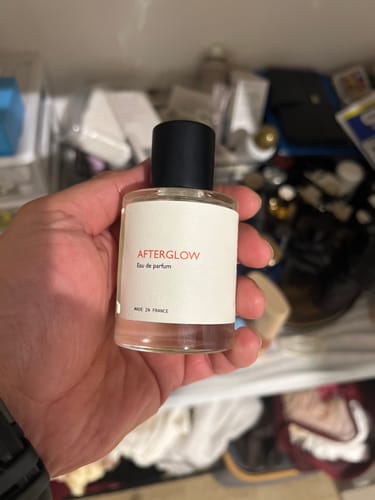 A person holding a clear glass bottle of Afterglow Eau de Parfum with a white label.