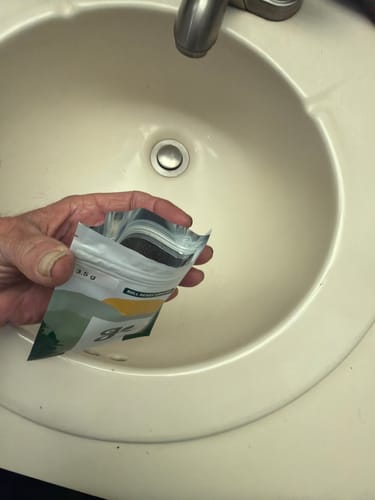 Customer holding an open pouch of Roll Ready Ground flower over a bathroom sink.