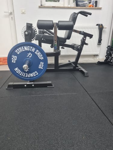 Reviewer's blue 20kg Strength Shop Calibrated Plate standing on the floor of a home gym.