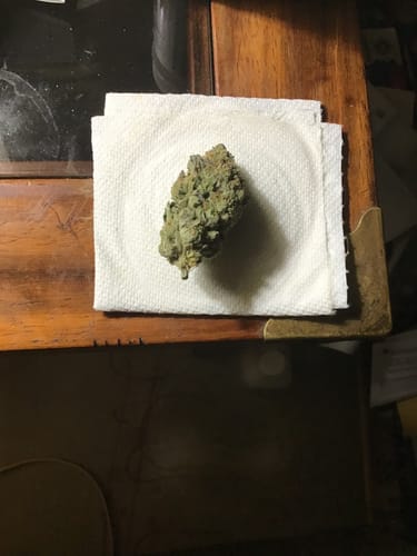 Reviewer's photo of a single green White Runtz bud resting on a paper towel on a wooden surface.
