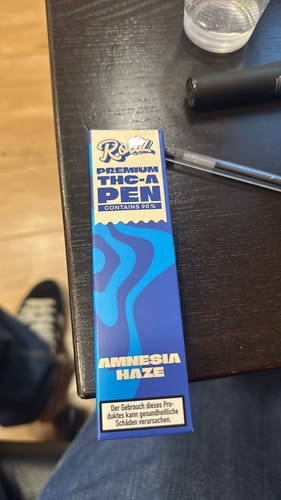 Customer's blue box for the ROLLZ Premium THC-A Pen, Amnesia Haze strain, on a dark wooden table.