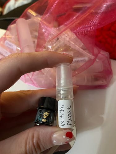 Customer holds a small sample vial of Witch, Please perfume with a handwritten label, next to a tiny decorative bottle.