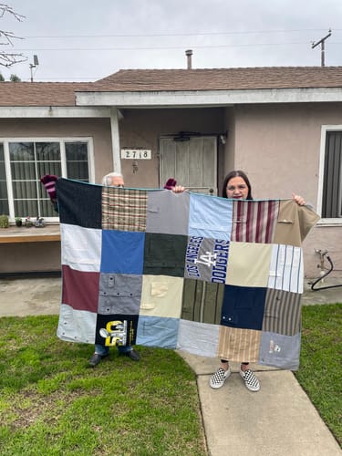 Customers holding their finished Premium T Shirt Quilt made from various button-up shirts and t-shirts outdoors.