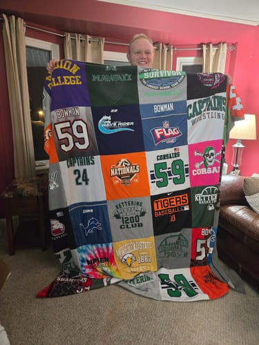 Customer holding up a large Premium T Shirt Quilt made from various colorful sports jerseys and shirts.