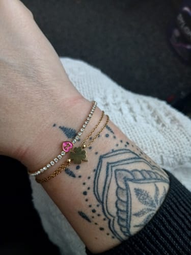 Close-up of a reviewer's wrist with a sparkling tennis bracelet and a gold charm bracelet over a tattoo.