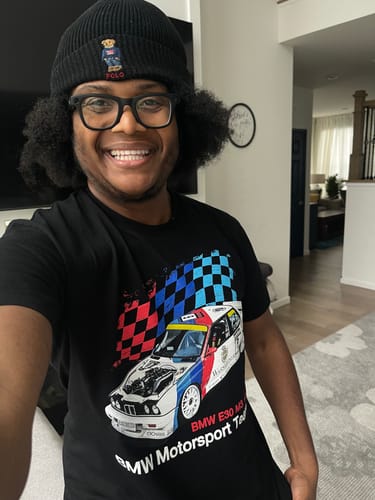 Reviewer smiling while wearing the black RACING DNA TEE with a prominent race car graphic.