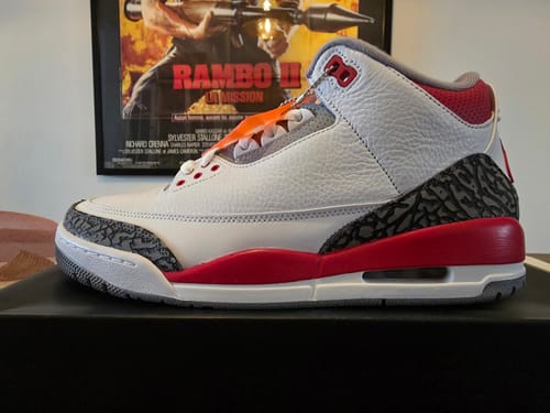 Recensent toont een ander zijaanzicht van de witte en rode Air Jordan 3 OG Fire Red sportschoen.