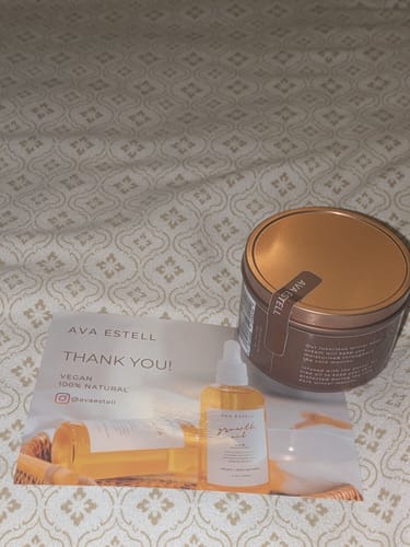 Customer's sealed Winter Body Cream tub with a gold lid, shown with a thank you card on a bedspread.