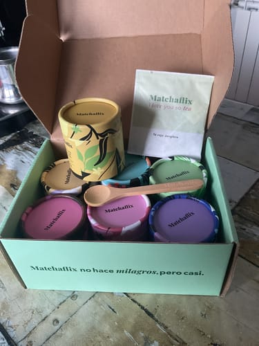 Cliente muestra la caja abierta del Pack Sabores de Té Matcha, que contiene varias latas de degustación coloridas y una cuchara.