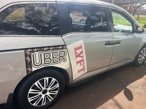 Customer's KOI SLAP sticker framing a homemade UBER sign on the side of a silver car.
