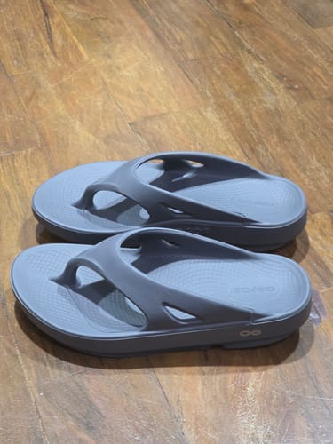 Customer's grey OOFOS OORIGINAL Thong sandals with thick soles, shown on a wooden floor.