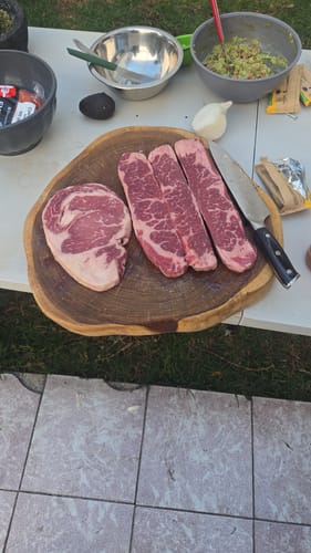 Cliente mostrando los cortes de carne cruda del Kit Parrillero sobre una tabla de madera antes de un asado.