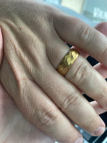 Close-up of a customer's hand wearing The Freya, a hammered gold wedding band, on their finger.