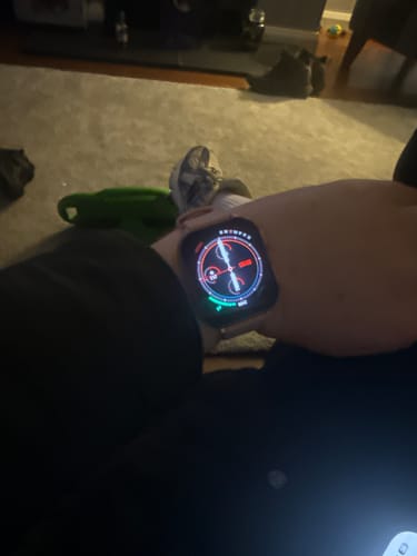 Close-up of a reviewer's wrist showing a smartwatch with a colorful, illuminated analog-style screen.