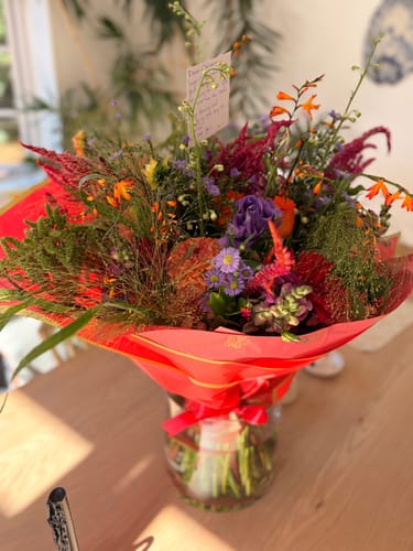 Customer's beautiful Wild and Free Bouquet wrapped in bright red paper and sitting in a vase on a wooden table.