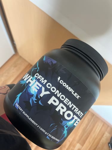 Customer holding a large black tub of Complex CFM Concentrate Whey Protein.