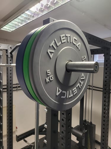 Ein Kunde zeigt seine farbigen Hantelscheiben auf einer Langhantel in einem Power Rack.