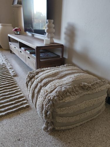 Recensent toont de naturelkleurige Lorena Canals Air poef in een woonkamer, die de nette en getextureerde afwerking benadrukt.