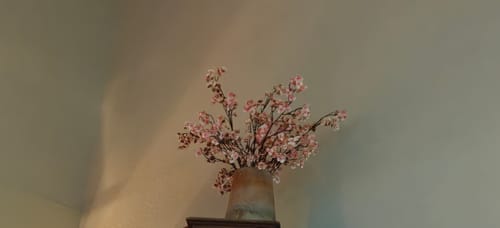 Beoordelaar toont een boeket roze kunstbloemen in een rustieke stenen vaas in een hoek.