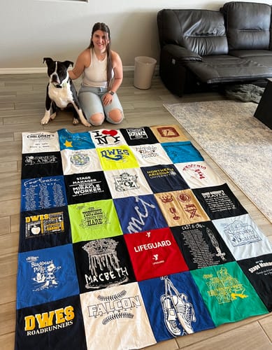 Customer kneeling with a dog beside a large, colorful Premium T Shirt Quilt displayed on a living room floor.