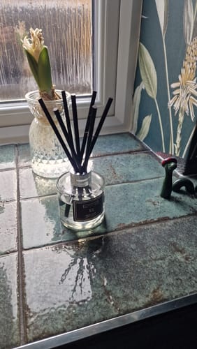 Customer's Reed Diffuser with black reeds on a tiled kitchen windowsill, next to a small plant.