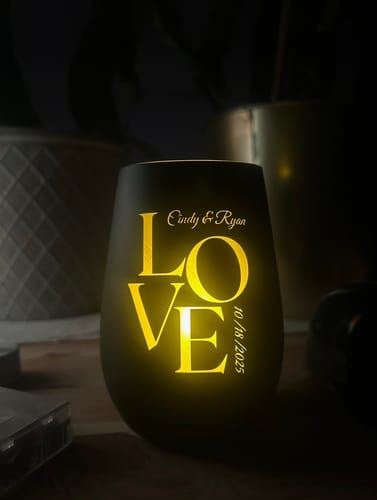 Kunde zeigt sein leuchtendes personalisiertes Windlicht, das mit Namen, Datum und dem Wort 'LOVE' graviert ist.