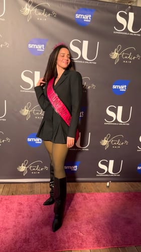 Customer wearing the Suiting Blazer Mini Dress with a pink sash and boots on a red carpet.