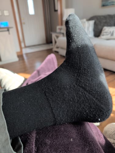 A customer's foot wearing a pilled black Performance Eucalyptus Compression Sock indoors.