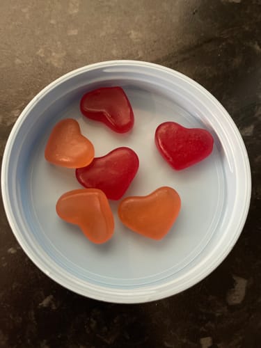 Reviewer's close-up of strawberry and peach heart-shaped Hormone Gummies in a container lid.
