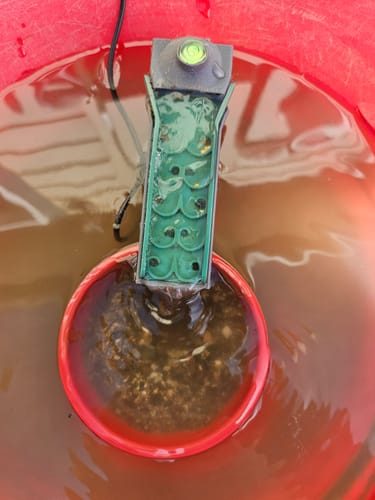 Customer's Keychain Highbanker Sluice operating in a red bucket, with water running down the green mat catching small flecks.