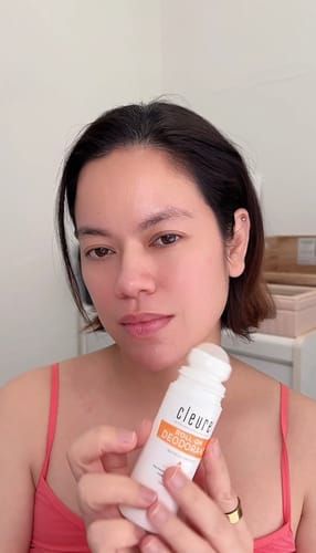 Reviewer holds up a white bottle of Cleure Roll-On Deodorant to the camera.