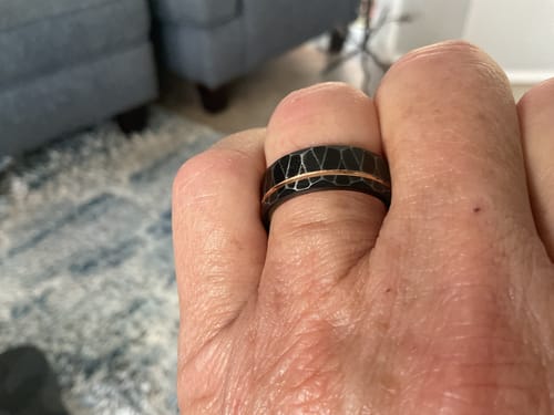 Customer's hand wearing The Stormlight ring, showing the black hammered texture and rose gold inlay.