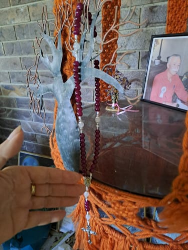Customer holding the garnet and chalcedony rosary, showing the red beads and crucifix draped over a home decoration.