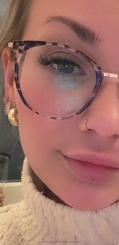 Kundin zeigt die voluminösen Heartbreak-Wimpern aus dem AMORE BUNDLE in einer Nahaufnahme mit Brille.