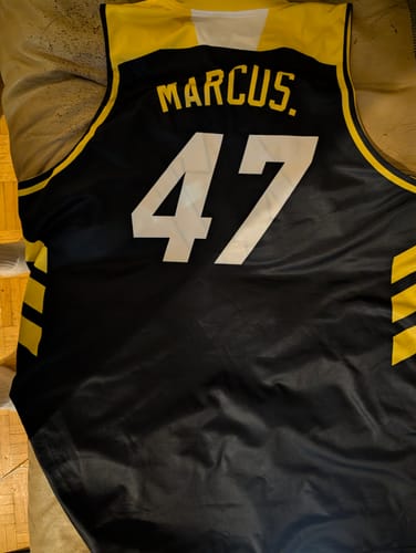 A customer's custom black and yellow basketball jersey laid out, showing the name "MARCUS." and the number "47" on the back.