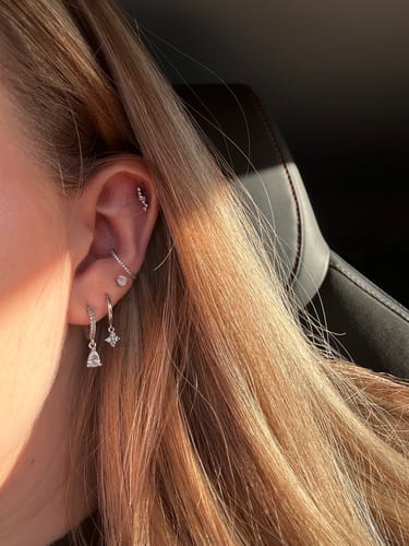 Close-up of a reviewer wearing the silver Amalfi Drop Huggies in their earlobe, styled with other piercings.