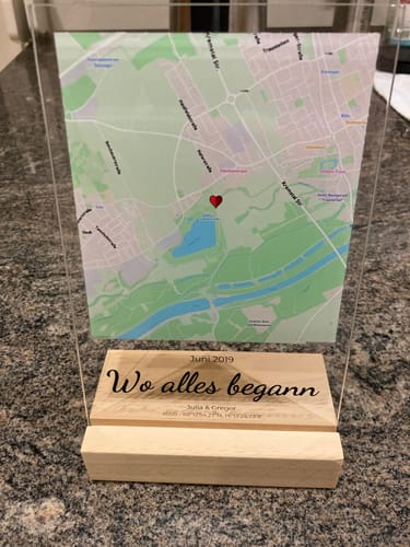 Kundenfoto der personalisierten Acryltafel 'Unser Ereignis', die mit einer Karte und einem gravierten Holzsockel auf einer Theke steht.