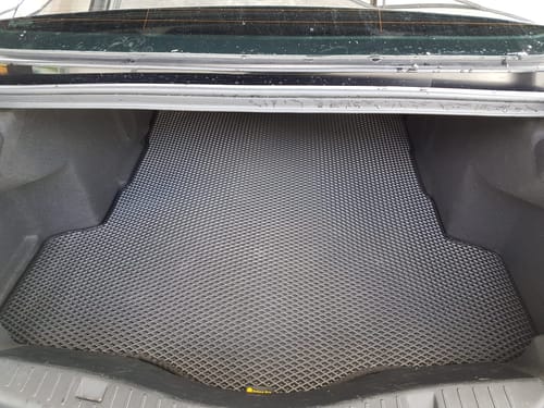 Recenzent pokazuje czarną matę do bagażnika o strukturze plastra miodu, dopasowaną do samochodu.