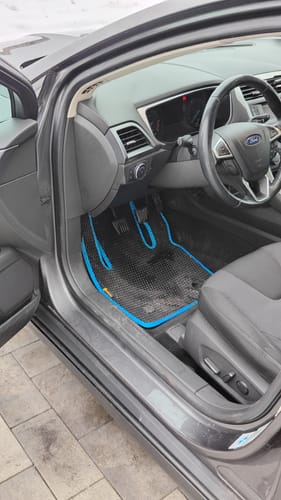 Zdjęcie recenzenta przedstawiające czarną matę podłogową z niebieskim obszyciem, dopasowaną do podłogi po stronie kierowcy.