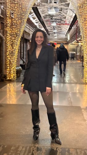 Customer smiling in an arched hallway, wearing the Suiting Blazer Mini Dress with tights and boots.