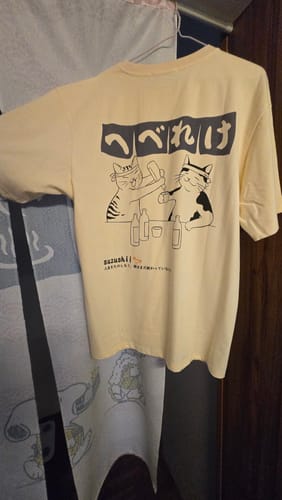 Customer's pale yellow Sake Night T-Shirt hanging up, showing the back graphic of two cats drinking.